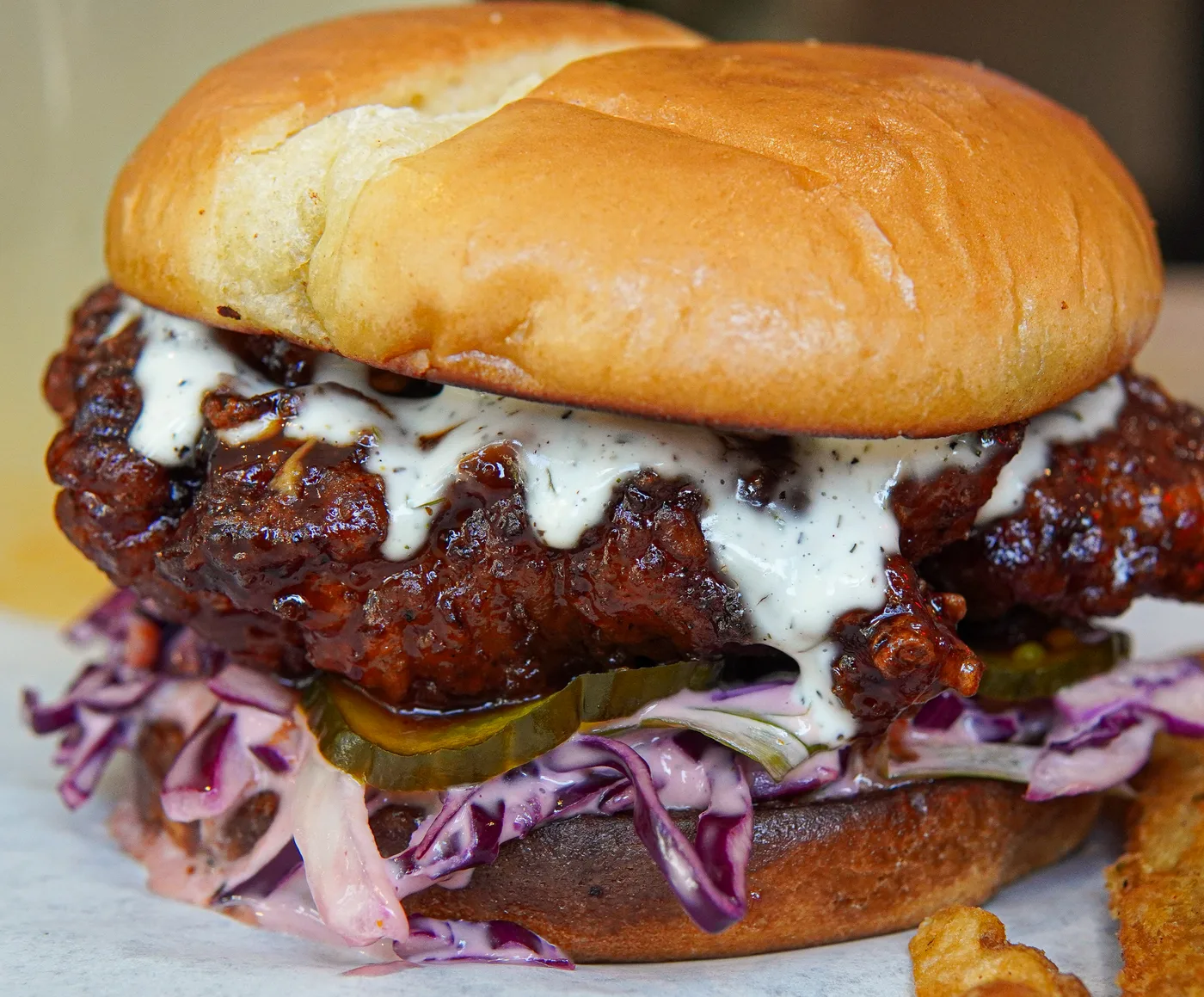 A fried chicken burger glazed in dark Yang-Yum sauce with ranch, pickles and purple coleslaw on a toasted brioche bun